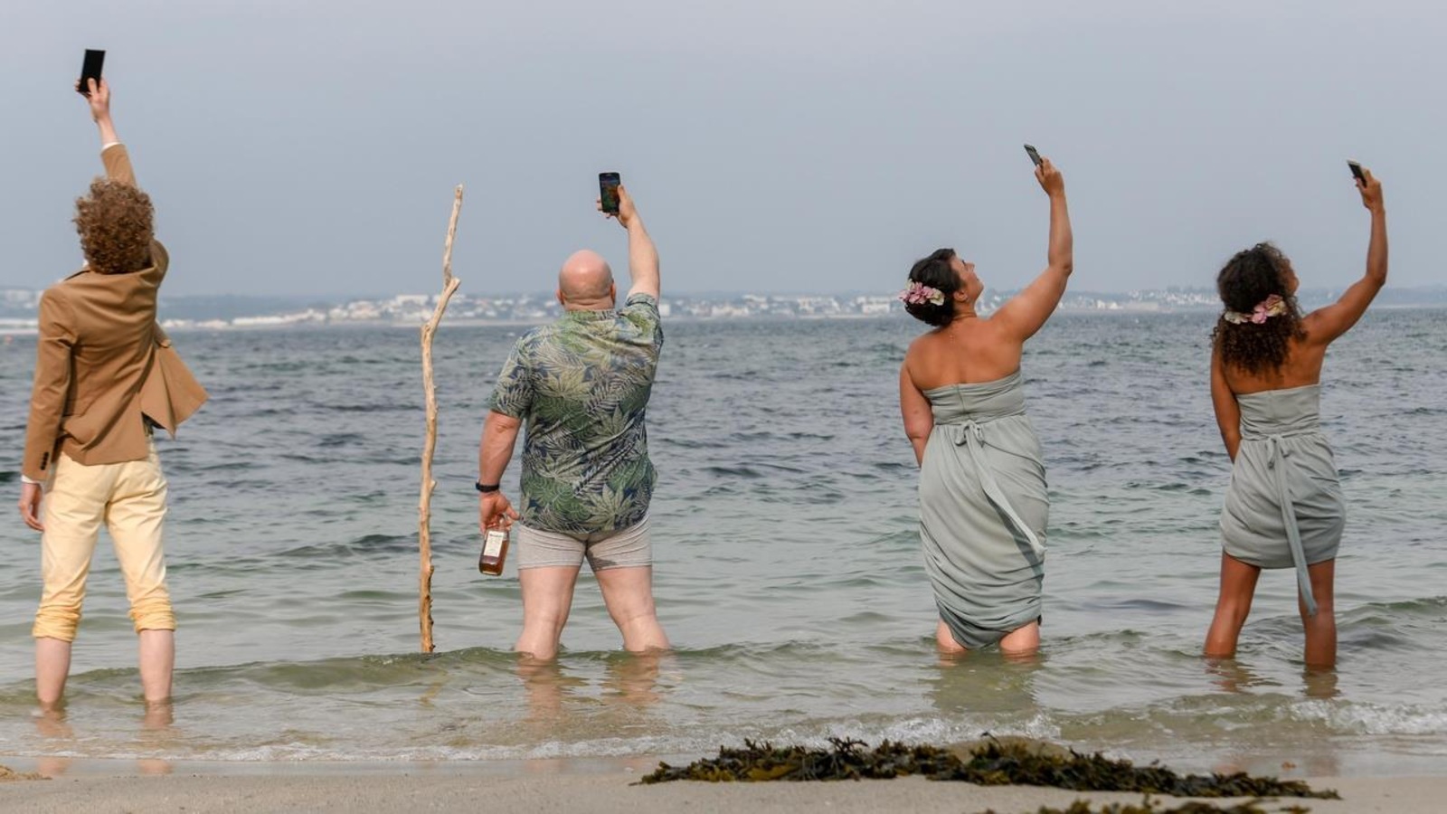 Deux hommes et deux femmes, de dos et face à la mer, prennent des autoportraits avec leurs téléphones. Deux hommes et deux femmes, de dos et face à la mer, prennent des autoportraits avec leurs téléphones.
