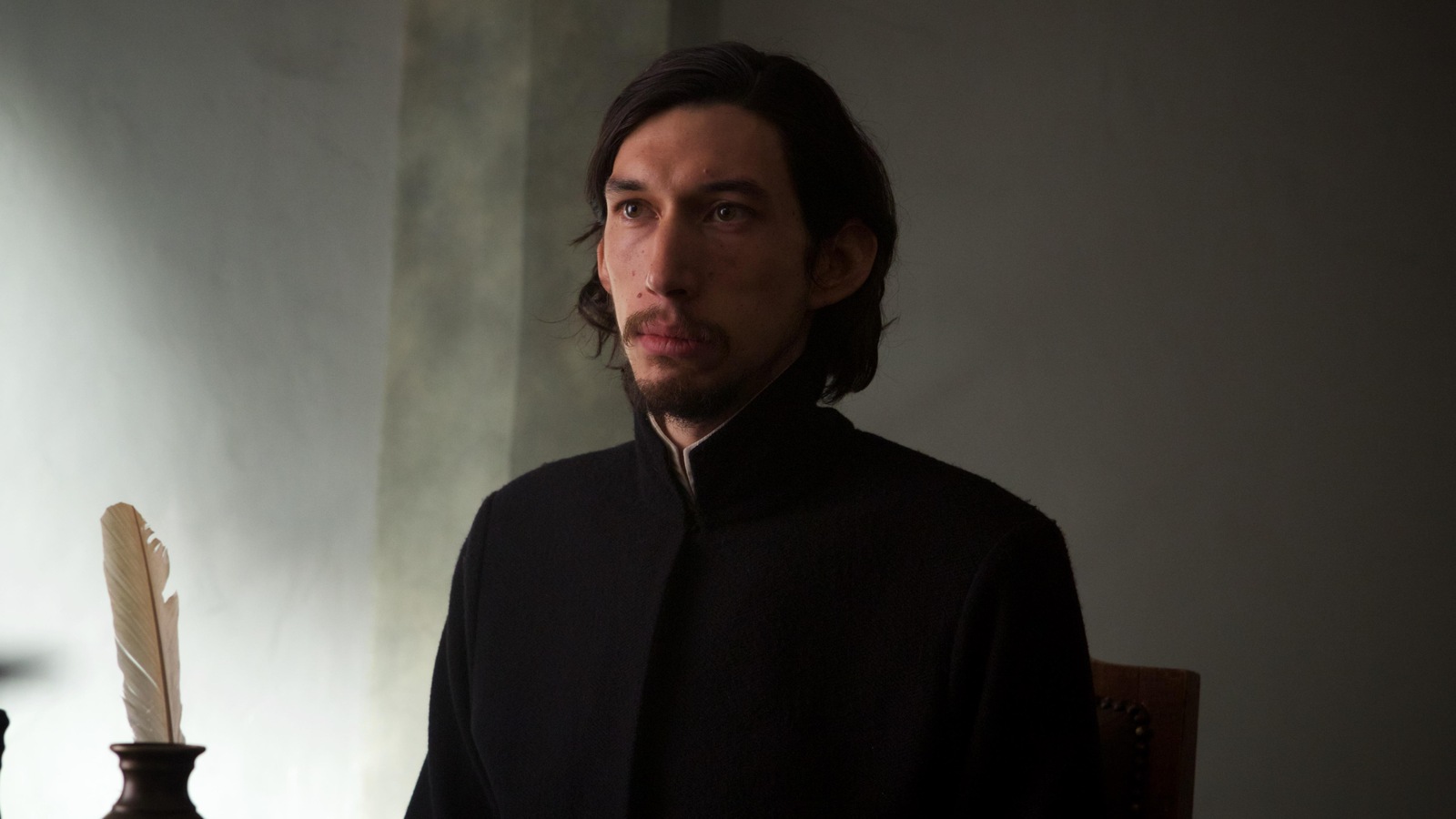 Un homme (Adam Driver) en tenue de prêtre, assis devant une plume d'écriture. Un homme (Adam Driver) en tenue de prêtre, assis devant une plume d'écriture.