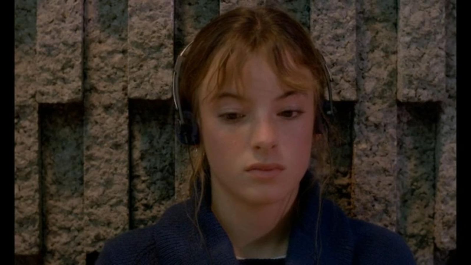 Une jeune fille (Pascale Bussières), devant un mur de pierres, le regard baissé, des écouteurs sur les oreilles. Une jeune fille (Pascale Bussières), devant un mur de pierres, le regard baissé, des écouteurs sur les oreilles.