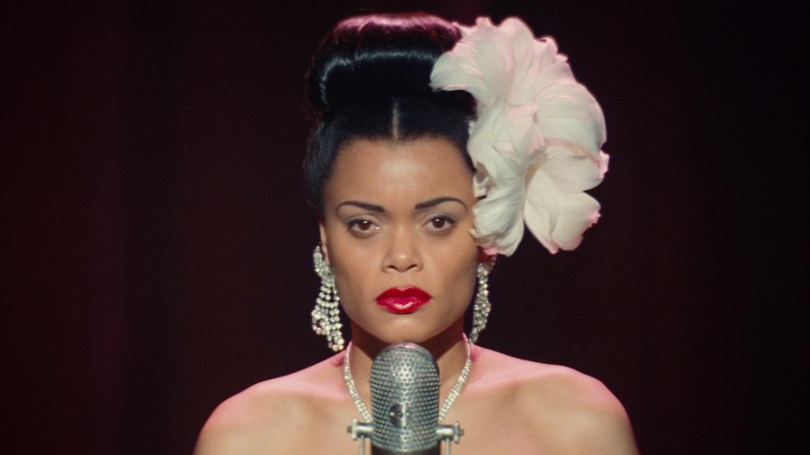 Une femme (Andra Day) avec une immense fleur blanche dans les cheveux, devant un micro. Une femme (Andra Day) avec une immense fleur blanche dans les cheveux, devant un micro.