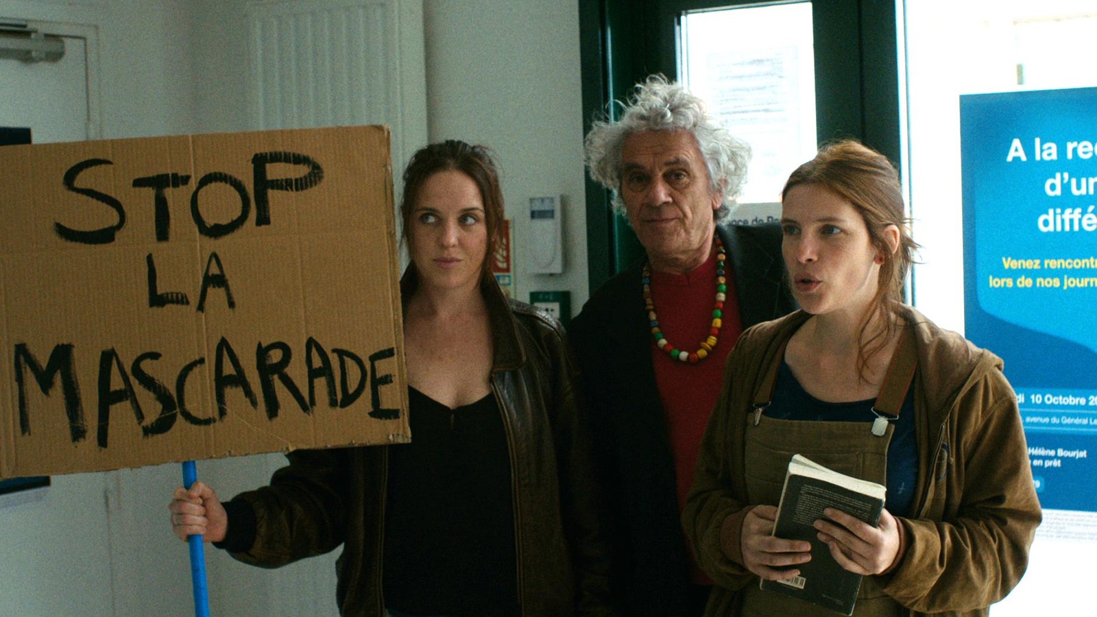 Deux femmes et un homme, avec une pancarte sur laquelle est écrit Stop à la mascarade.