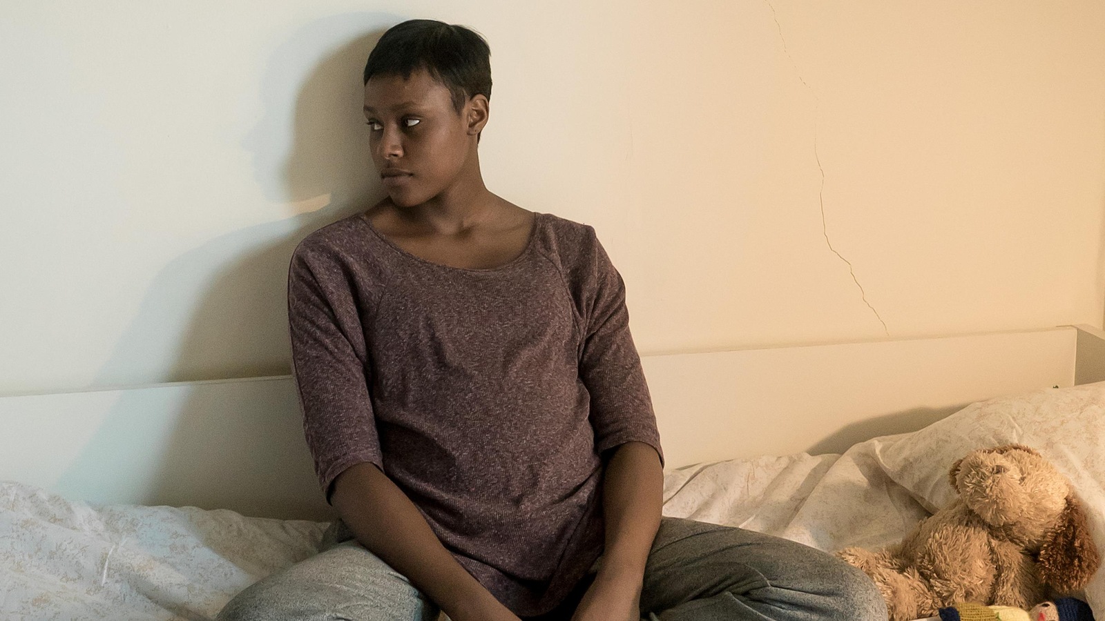 Edwidge (Naïla Victoria Louisdort-Biassou) est assise les jambes croisées sur son lit. Edwidge (Naïla Victoria Louisdort-Biassou) est assise les jambes croisées sur son lit.