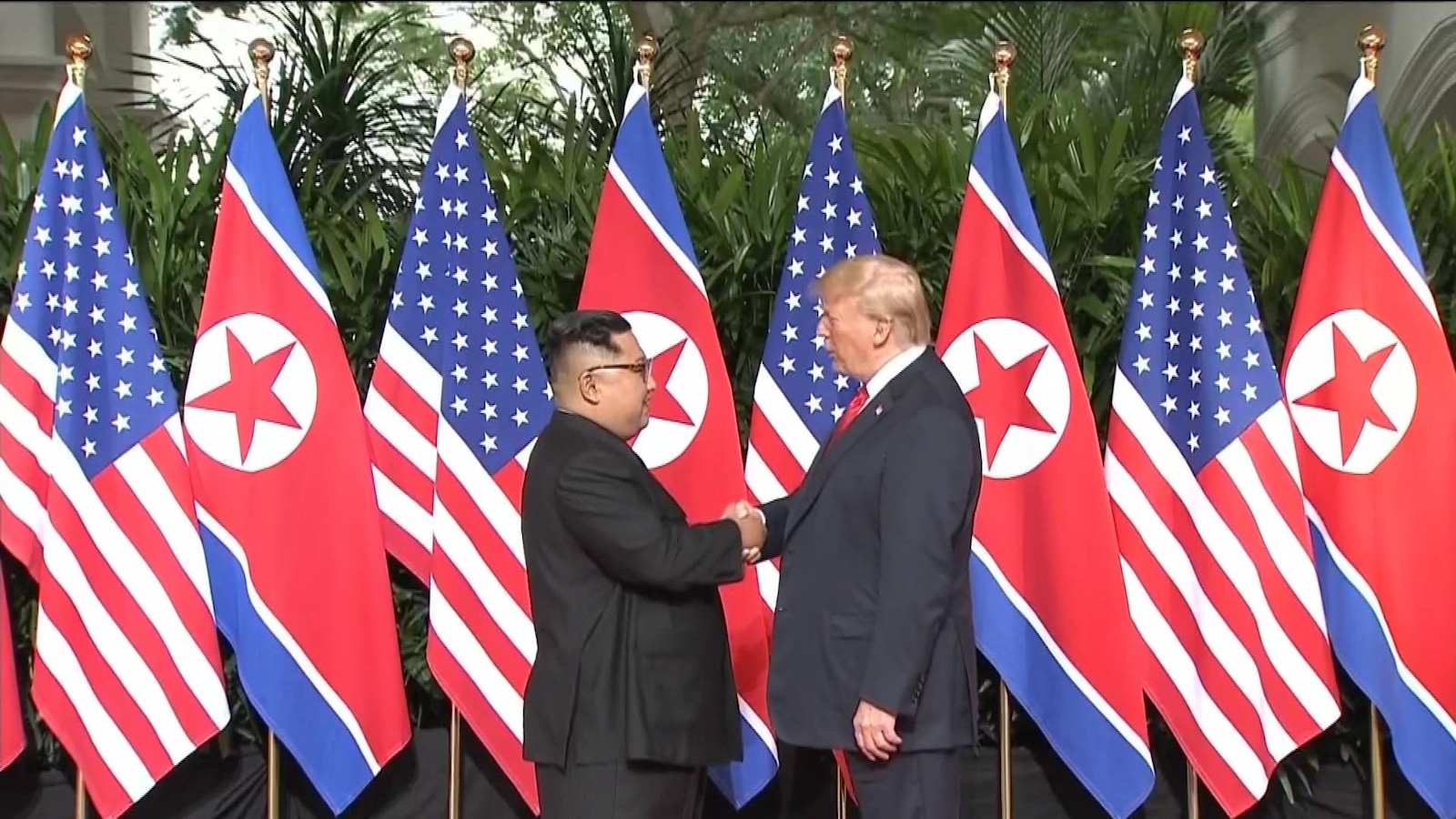 Donald Trump et Kim Jong-un se serrent la main devant des drapeaux de leurs pays respectifs. Donald Trump et Kim Jong-un se serrent la main devant des drapeaux de leurs pays respectifs.