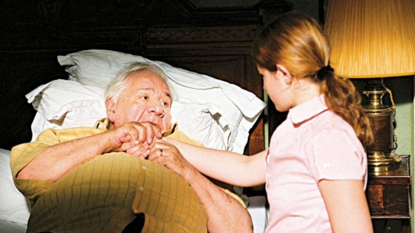Un vieil homme allongé sur un lit, une petite fille à côté de lui lui tient la main. Un vieil homme allongé sur un lit, une petite fille à côté de lui lui tient la main.