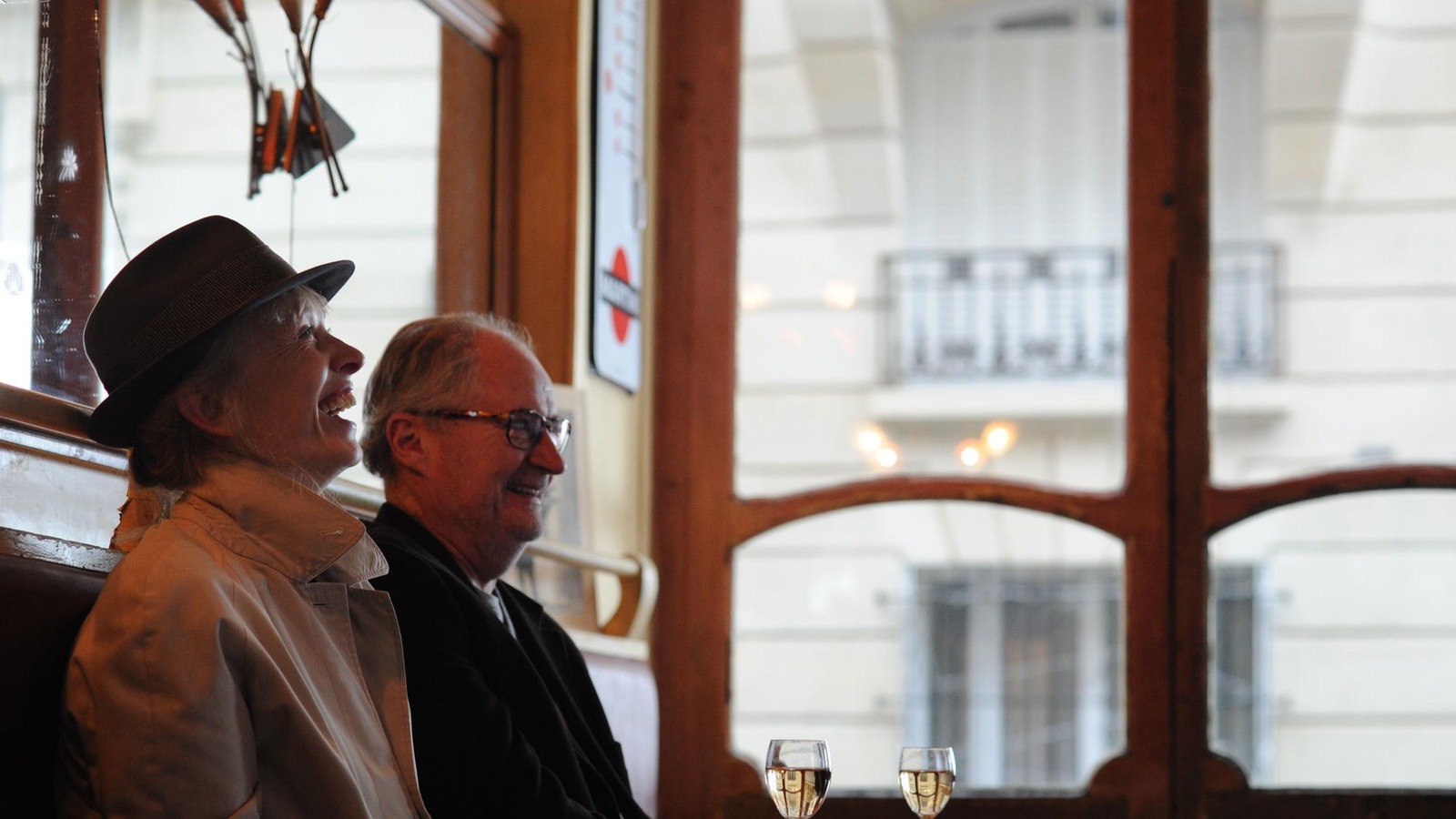 Un homme et une femme, assis côte à côte dans une brasserie parisienne, rient.
