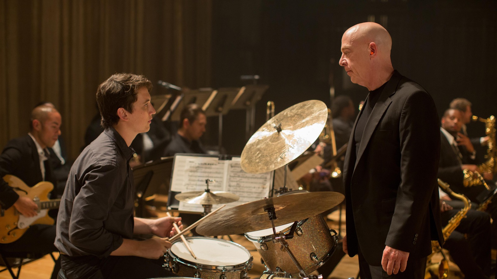 Un jeune batteur (Miles Teller) assis derrière son instrument, face à un homme en complet noir (J.K. Simmons) Un jeune batteur (Miles Teller) assis derrière son instrument, face à un homme en complet noir (J.K. Simmons)