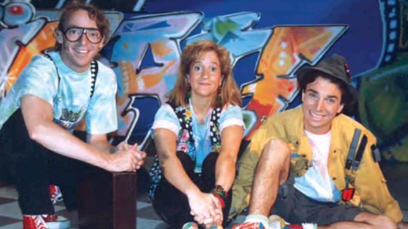 Les trois animateurs sont assis devant un mur de graffitis. 