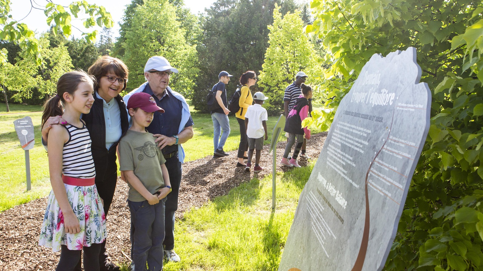 Sur le sentier du Jardin botanique, une famille lit un panneau explicatif de l'exposition. Sur le sentier du Jardin botanique, une famille lit un panneau explicatif de l'exposition.