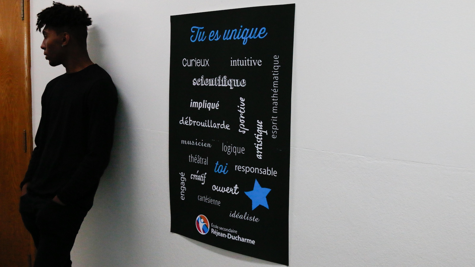 Un jeune est adossé au mur, on voit une affiche avec les valeurs du Collège Un jeune est adossé au mur, on voit une affiche avec les valeurs du Collège
