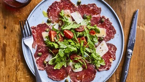Une assiette de carpaccio de bœuf garni de câpres, de feuilles de roquette, de copeaux de parmesan et de
tomates cerises.

