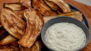 Des chips d'aubergines dans une assiette avec un bol rempli de tzatziki au labneh.