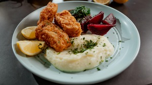 Des croquettes de morue dans une assiette avec des betteraves, de la purée de pommes de terre et des quartiers de citron.