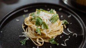 Une petite quantité de spaghettis aux courgettes garnie de basilic et de fromage râpé.