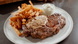 Un steak dans une assiette recouvert de sauce au poivre avec des frites et un petit pot de mayonnaise.