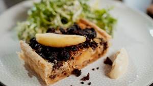 Un morceau de tarte au boudin, aux pommes et aux oignons dans une assiette avec une salade.