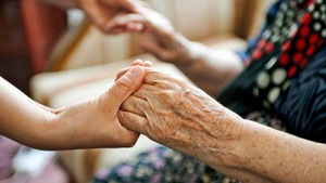Une personne et une aînée se tiennent les mains.