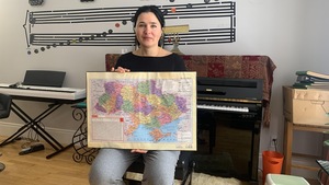 Une femme assise devant un piano tient une carte de l'Ukraine.