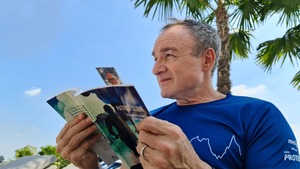 Devant un palmier, l'homme tient un livre entre ses mains et regarde l'horizon.