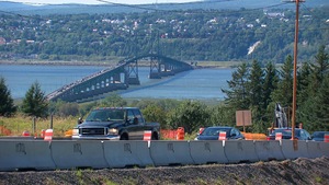 Des voitures circulent dans une zone de construction. Le pont congestionné est visible au loin.