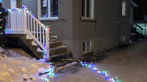 Des lumières de Noël au sol devant une maison grise le soir.