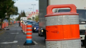 Des cônes orange délimitant une zone de travaux à Montréal, avec une file de véhicules à droite.