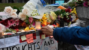 Un homme allume une bougie sur un muret où ont été déposés fleurs et messages.