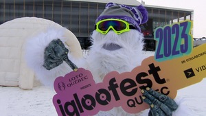 La mascotte Yeti, portant des lunettes de ski et une tuque, pointe vers une pancarte de l'événement qu'elle tient dans ses mains.