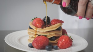 Une femme verse du sirop d'érable sur des pancakes et des petits fruits.