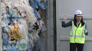 Une femme parle aux journalistes devant un conteneur rempli de sacs de plastique.