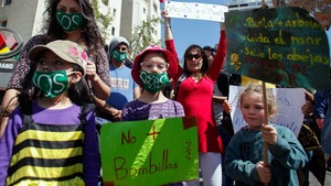 Des enfants, dont le plus jeune semble avoir environ 7 ans, manifestent entourés de leurs parents, en tenant des pancartes et en arborant un masque sur la bouche où il est écrit S.O.S.