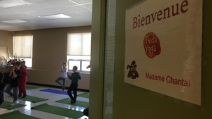 Une pancarte sur une porte souhaite la bienvenue dans la classe de Peda Yoga. Des élèves pratiquent le yoga en arrière-plan