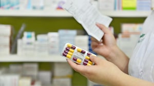 Une pharmacienne tient une ordonnance dans une main et une plaquette de médicaments dans l'autre