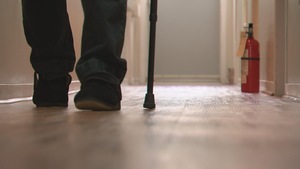 Un aîné marche dans un couloir à l'aide d'une canne.