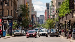 Des voitures et des piétons circulent sur une rue commerciale au centre-ville de Montréal.
