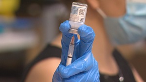 Une main gantée tenant une seringue puise une dose de vaccin dans une fiole.