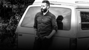 Le musicien est adossé sur une mini-fourgonnette blanche.