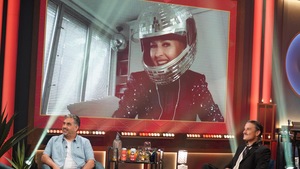 Sur écran géant, Geneviève Borne porte un casque de moto décoré style boule disco en miroir.