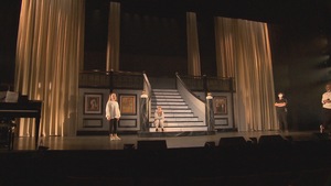 Quatre personnes sur une scène avec un escalier de marbre et de long rideaux blancs.