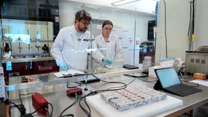 Deux scientifiques portant des sarraus et gants dans un laboratoire.