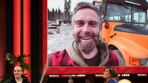 Un homme qui sourit. Derrière lui, un autobus scolaire.