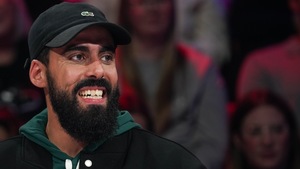 L'homme porte une casquette et est assis en studio.
