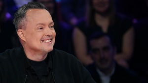 Il est assis en studio et rit.