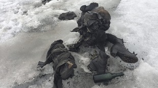 Des restes de vêtements, de souliers et une bouteille en verre sur la neige