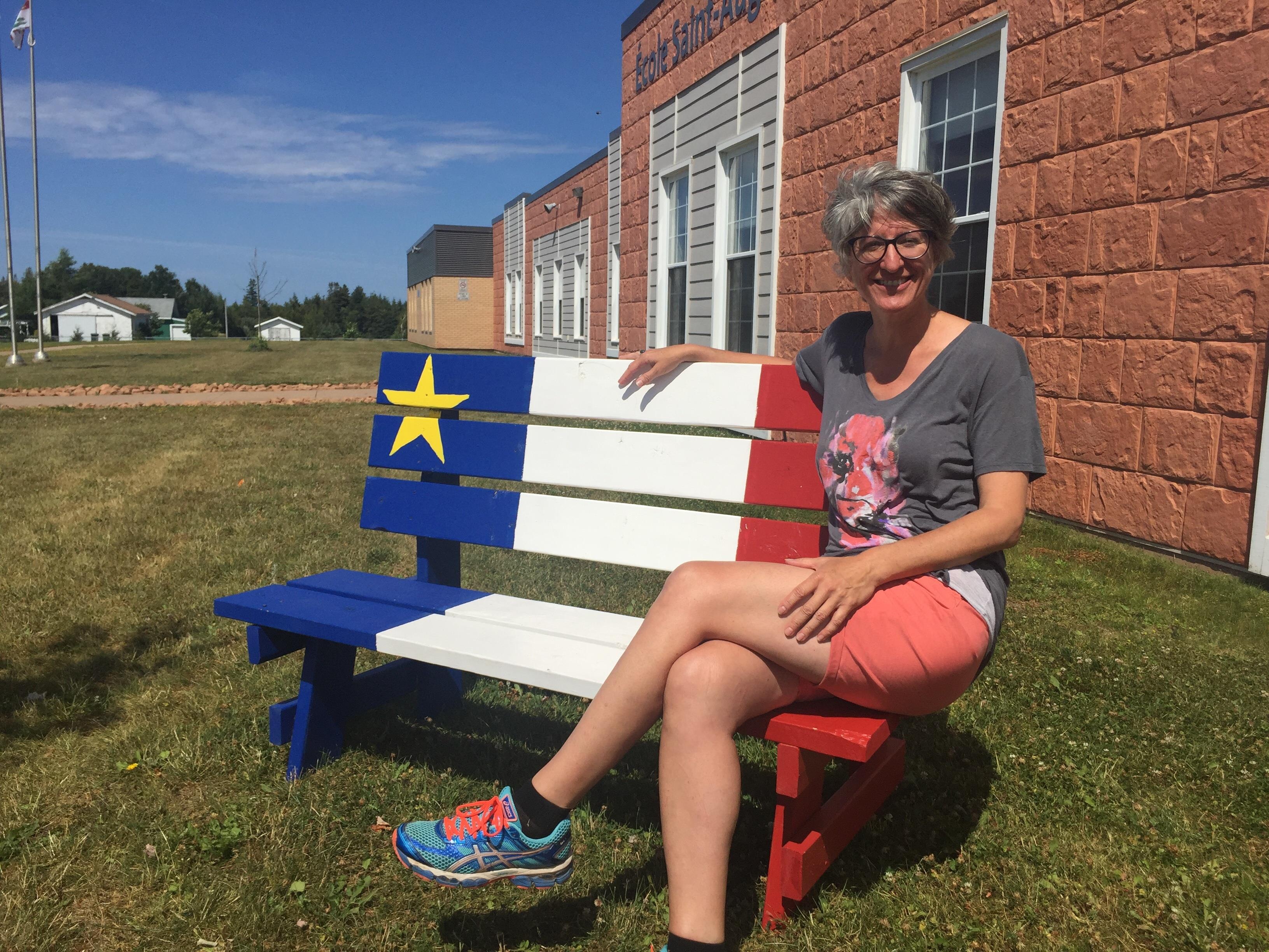 Andréa Deveau est assise sur un banc peint aux couleurs de l'Acadie. Andréa Deveau est assise sur un banc peint aux couleurs de l'Acadie.