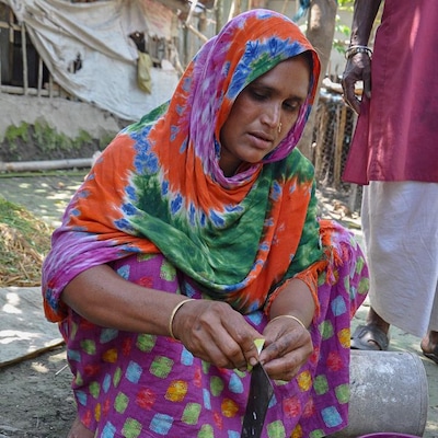 Une femme portant un voile multicolore est accroupie et tranche de petites mangues vertes.