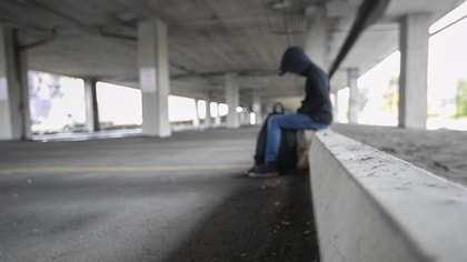 Un adolescent assis sous un pont, la tête penchée. 