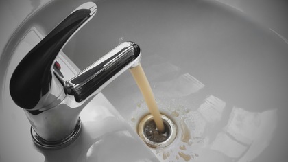 Un robinet qui d'où s'écoule de l'eau brune.