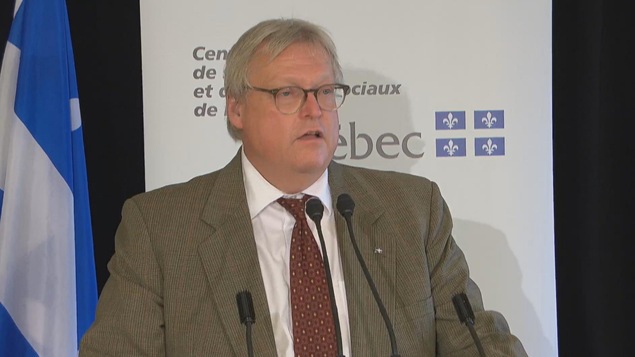 Gaétan Barrette en conférence de presse. Derrière lui se trouve le drapeau du Québec.