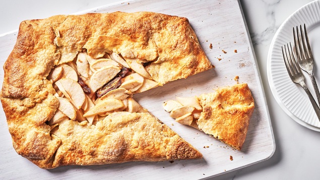 Une tarte rustique aux pommes, aux poires et aux dattes dans une assiette avec une part déjà coupée.