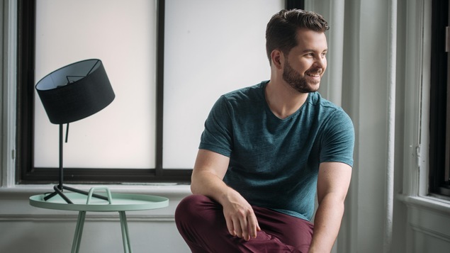 Le chef d'orchestre Simon Rivard, assis, la tête tournée vers la droite.